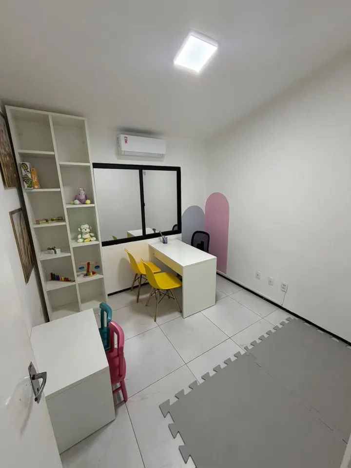 Sala de atendimento com mesa, cadeiras infantis, estante de brinquedos e tatame